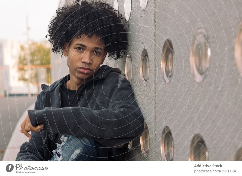 Teen ethnic man with curly hair sitting on street hipster teenage urban serious young afro modern male african american black millennial lifestyle adolescent