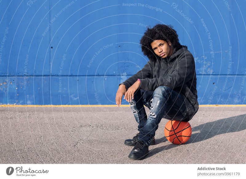 Hipster black adolescent sitting on basketball man hipster teen serious streetball young confident style male informal african american ethnic afro curly hair