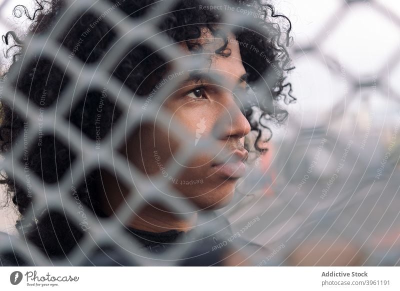 Young ethnic man behind wire fence thoughtful serious teen pensive young curly hair human face male chain link african american black teenage adolescent barrier