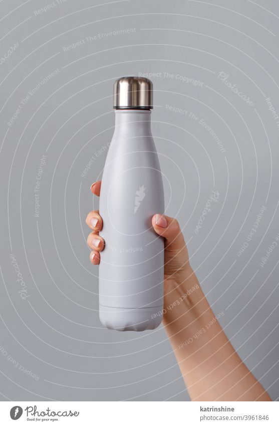 Close up of female hand, holding grey reusable bottle on grey background woman monochrome mockup yellow insulated ecologic water steel thermo aluminum blank