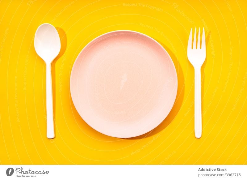 Kit of disposable tableware on yellow background plastic plate fork spoon utensil set dishware empty kit cutlery dinnerware simple color minimal tool serve item