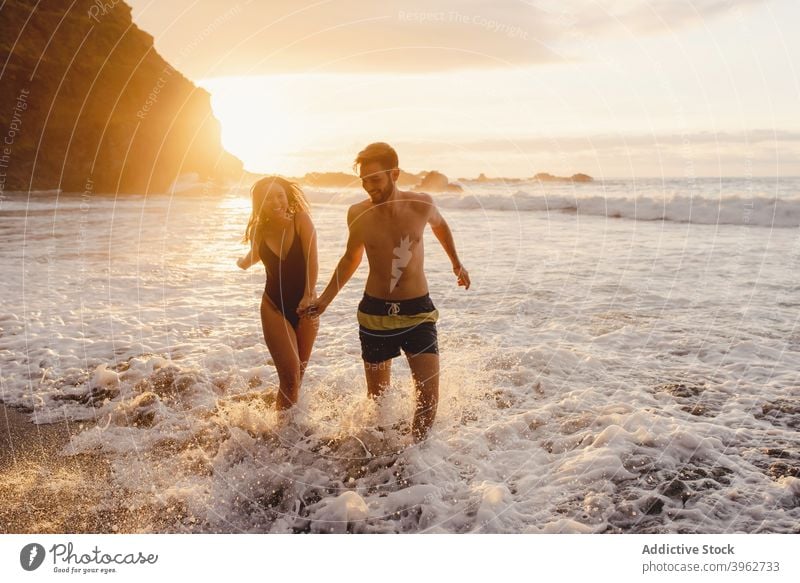 Romantic couple walking on foamy sea waves sunset romantic love beach together happy ocean having fun holding hands coast fondness young tenerife island canary