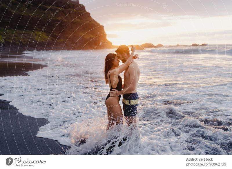 Happy couple having fun in foamy sea waves romantic love beach together happy sunset water fondness young tenerife island canary spain embrace relationship