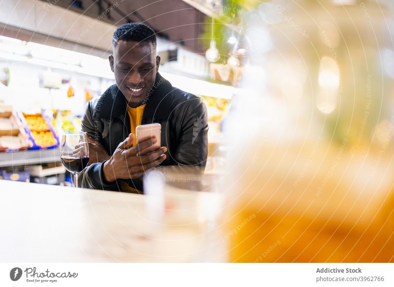 Black man browsing smartphone in cafe cheerful social media message wine chill weekend male black african american ethnic table glass mobile surfing connection