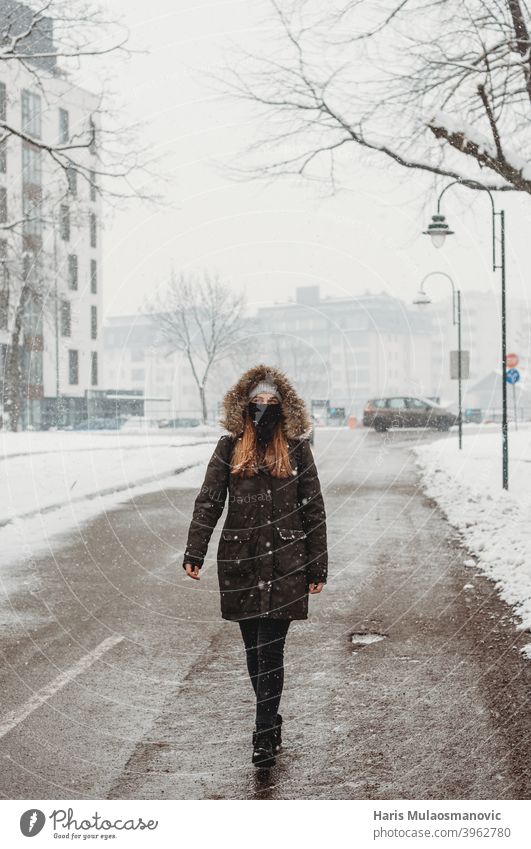 woman with face mask walking outdoors in snow adult alone attractive beautiful black brunette cold confident coronavirus covid-19 cute empty empty city fashion