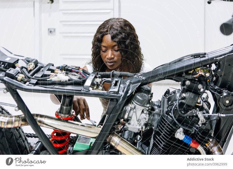 Black woman repairing motorcycle in garage mechanic fix motorbike workshop wrench spanner service female ethnic black african american technician custom