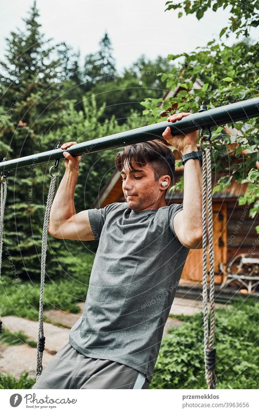 Young man doing pull-ups on pull-up horizontal bar during his calisthenics workout on a camping during his summer vacation active activity athlete athletic body