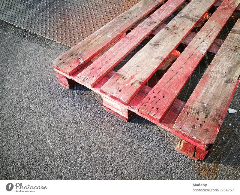 Red and pink stained old wooden pallet on checker plate and grey asphalt in sunshine in the yard of a factory in Oerlinghausen in Ostwestfalen-Lippe, Germany