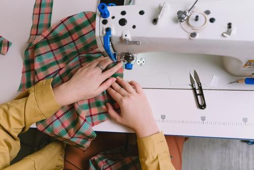 Top view of woman working with sewing machine in her workshop fabric tailor material seamstress clothing needle craft thread textile business worker dress