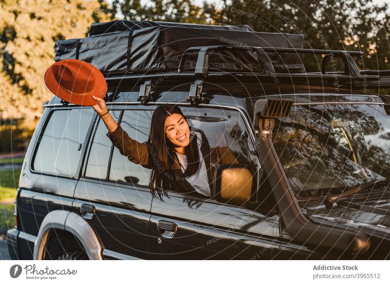 Delighted ethnic traveler in car woman peep wave hand cheerful automobile window vacation trip female asian australia road trip outstretch arm holiday enjoy