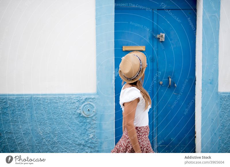 Anonymous stylish female standing near door of typical house on sunny day woman fashion style vacation architecture facade tourist young trendy straw hat cozy