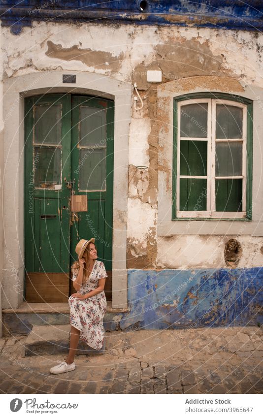 Female traveler sitting on the street near old building in Algarve woman house doorstep happy sightseeing summer holiday female cheerful young blond dress