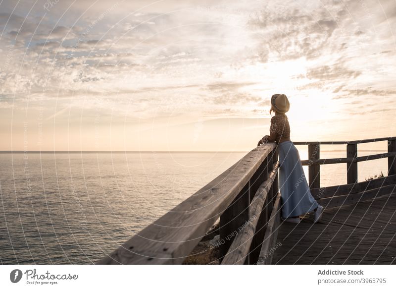 Anonymous female tourist enjoying seascape while recreating on wooden promenade woman relax pier admire sunset nature traveler style alone recreation young