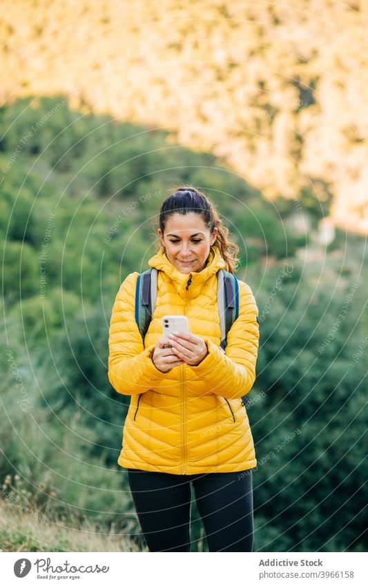 Traveling woman in outerwear using smartphone in nature hiker browsing trekking season hill surfing female mobile smile travel adventure warm jacket