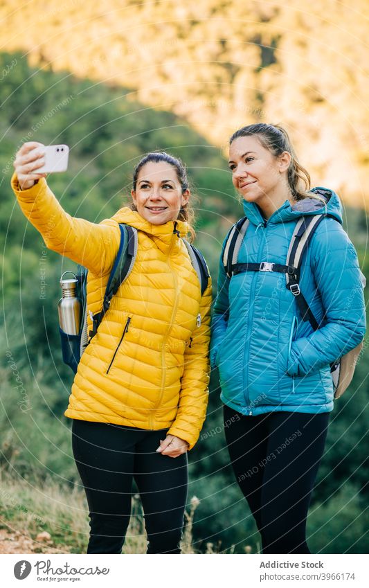 Smiling traveling women taking selfie in nature trekking hiker together smartphone female smile young gadget mobile joy cheerful device optimist memory backpack