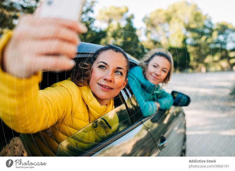 Women taking selfie in car women together friend self portrait automobile smartphone peep road smile female friendship window happy gadget device memory joy