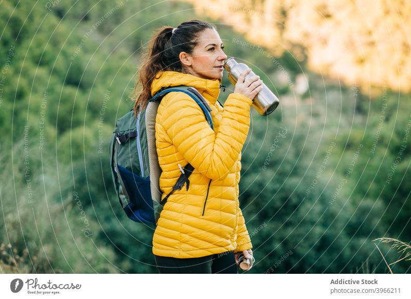Traveling woman drinking water in nature hiker trekking bottle season thirst hydrate female warm jacket travel young metal adventure journey activity tourist
