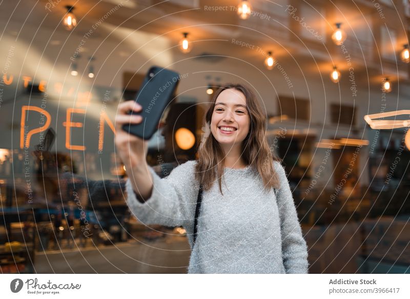 Cheerful woman taking selfie on smartphone in city cheerful weekend self portrait charming smile take photo female cafe window mobile happy glad relax joy young