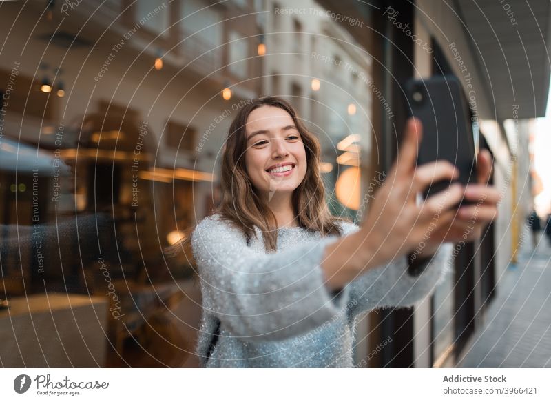 Cheerful woman taking selfie on smartphone in city cheerful weekend self portrait charming smile take photo female cafe window mobile happy glad relax joy young