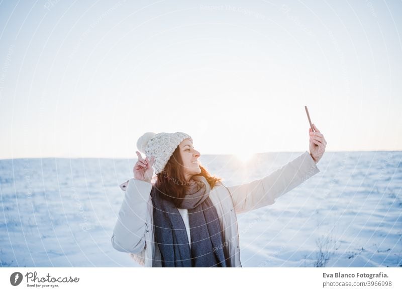 beautiful young woman at sunset in snowy mountain using mobile phone. Nature and technology concept. winter season hiking cold covered caucasian forest