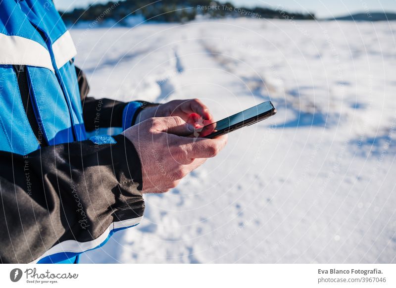 close up of man hiking in snowy mountain in a sunny day using mobile phone. Technology and Nature. winter season technology cold covered caucasian forest
