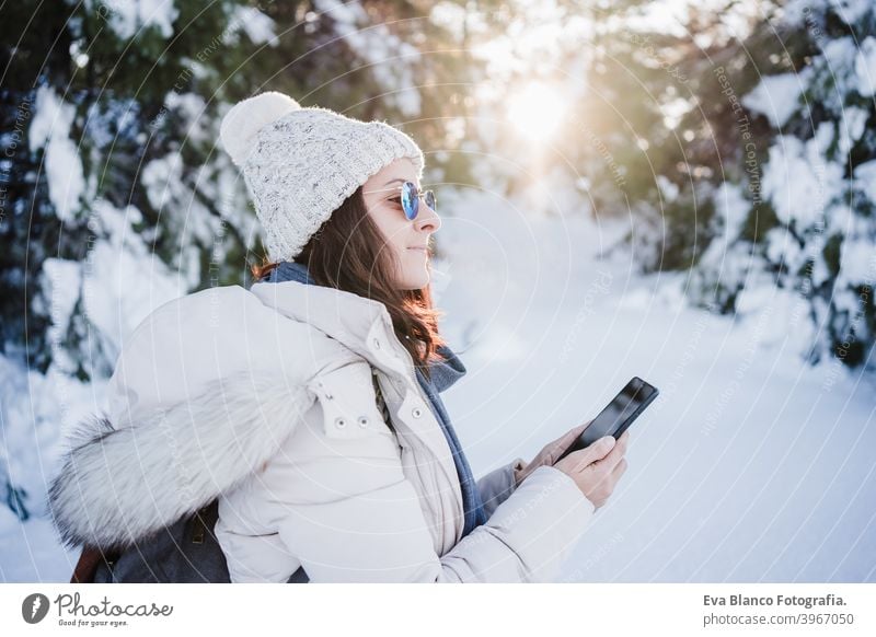 beautiful young woman at sunset in snowy mountain using mobile phone. Nature and technology concept. winter season hiking cold covered caucasian forest