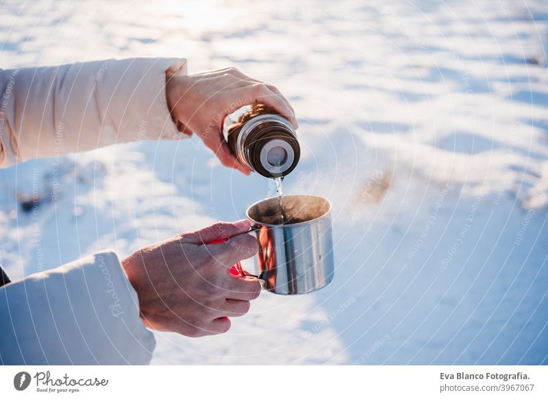 unrecognizable beautiful young woman at sunset in snowy mountain pouring hot tea from thermos to metallic cup. Travel and Nature concept. winter season drink