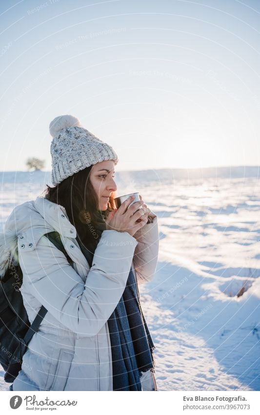 beautiful young woman at sunset in snowy mountain holding a cup of hot tea. Travel and Nature concept. winter season thermos drink hot water sunny hiking cold
