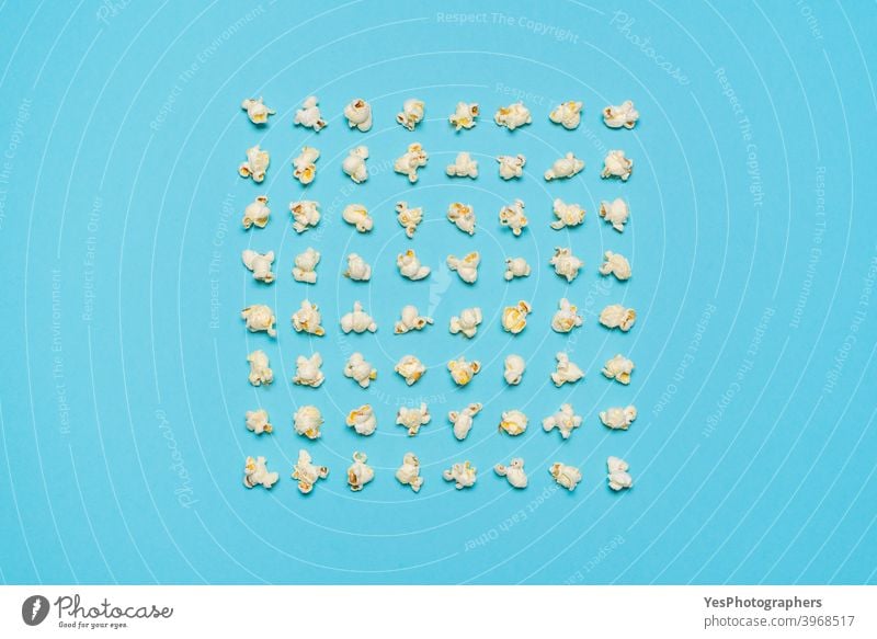 Popcorn flakes aligned symmetrically on a blue background. above view american appetizer arranged cinema classic comfort food container cut out delicious