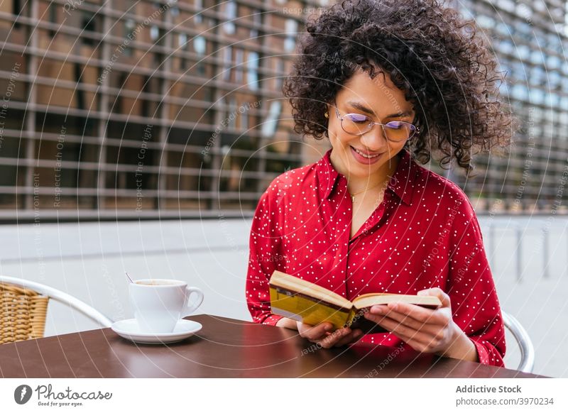 Happy woman reading book on cafe terrace happy coffee rest enjoy young positive ethnic curly hair hispanic female eyeglasses interesting lifestyle free time