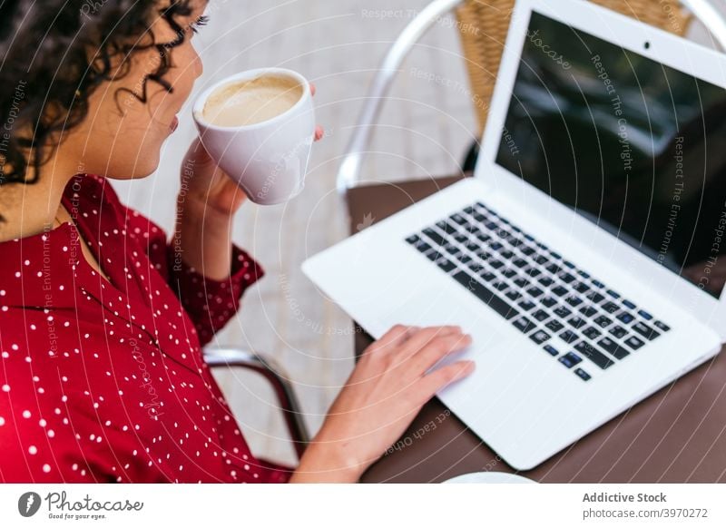 Anonymous woman with laptop and drinking coffee sitting on cafe terrace pensive work remote freelance young ethnic hispanic businesswoman female device gadget