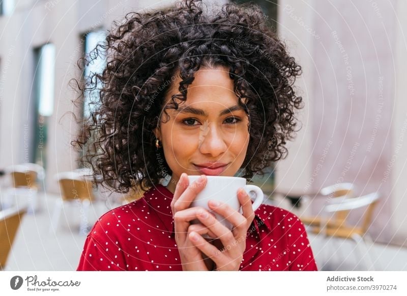 Smiling ethnic woman drinking coffee in street cafe enjoy happy curly hair young cup rest female aromatic beverage cheerful lifestyle relax smile positive