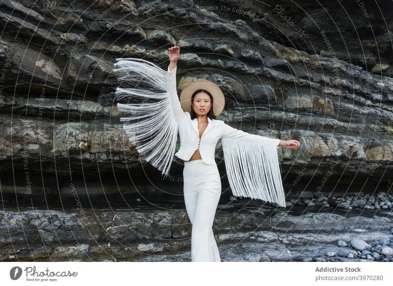 Stylish woman in fashionable wear standing near rock style elegant outfit white wing model tassel suit hat young asian female ethnic trendy slim vogue feminine