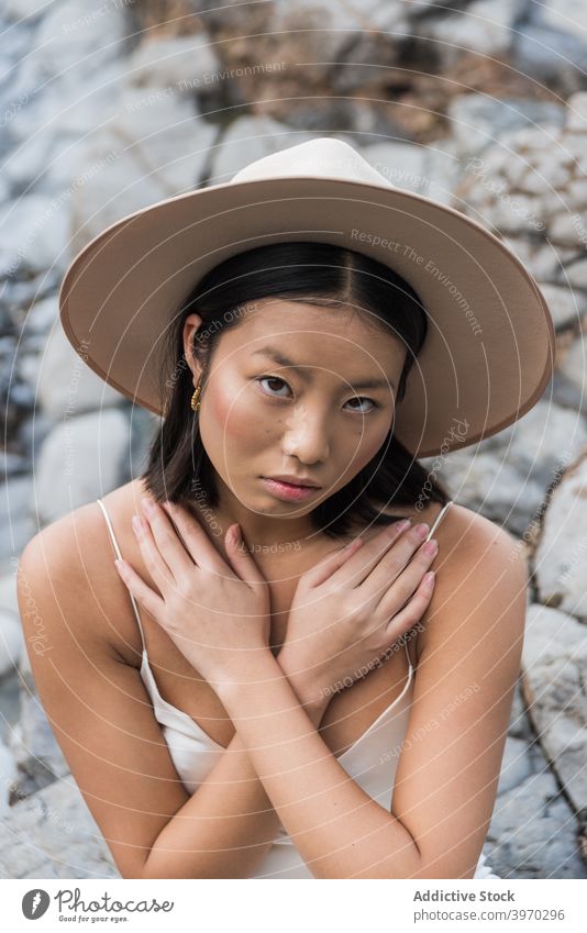 Young ethnic female in hat standing on stones woman style fashion cover young summer rocky model vogue asian headgear headwear cold attractive sensual pure