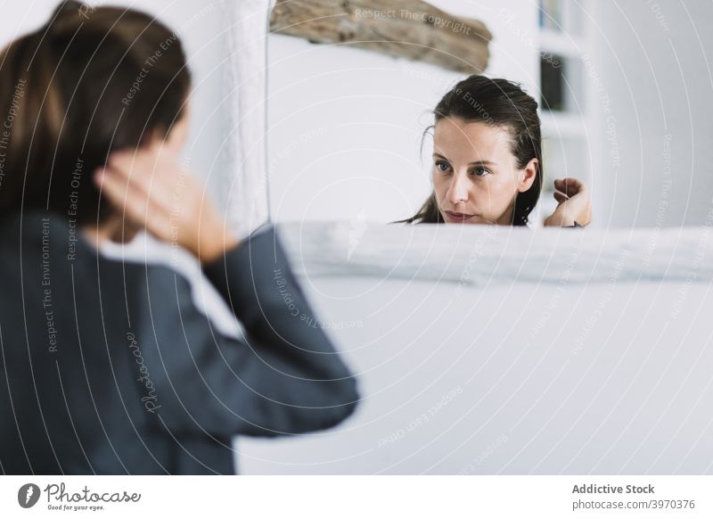Young woman adjusting hair in front of mirror thoughtful prepare morning formal routine reflection touch hair young female businesswoman everyday confident