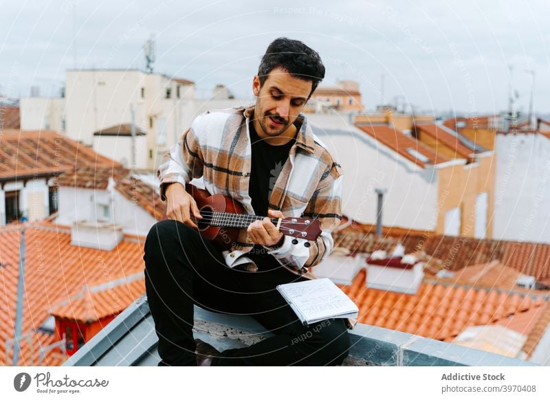 Man with ukulele composing music on rooftop man play instrument compose melody song acoustic male ethnic building concentrate guitar perform musician guitarist