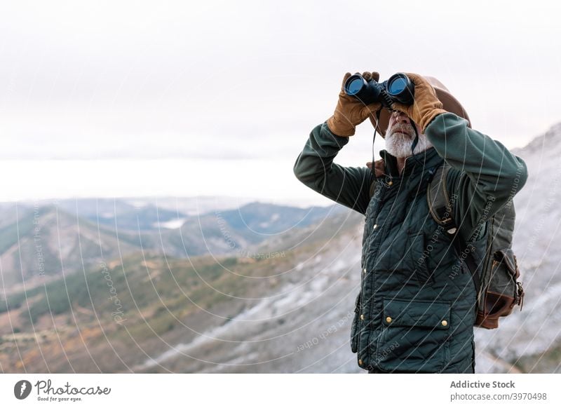 Elderly man looking through binoculars in mountains traveler observe admire highland winter senior outerwear male caceres extremadura spain picturesque terrain