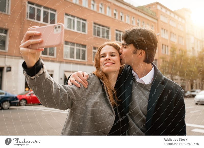 Loving young couple taking selfie on street love kiss together happy smartphone relationship embrace girlfriend boyfriend cheerful lifestyle romantic affection
