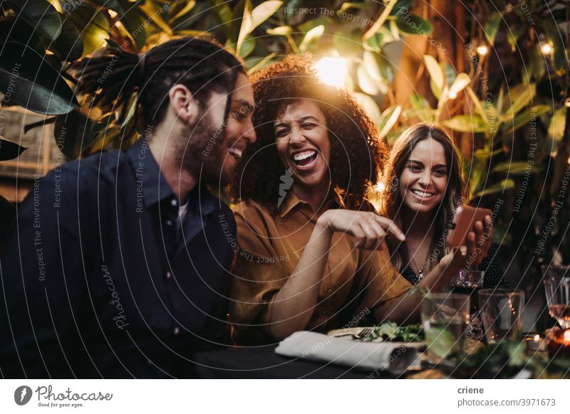 Young adult friends laughing and having fun at dinner party with phone Candid Happiness Smartphone Smiling Young Adult african american african ethnicity