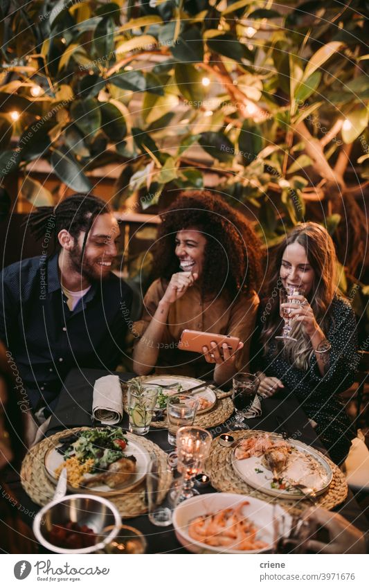 Diverse group of friends laughing and having fun with phone at garden dinner party Candid Happiness Smartphone Smiling Young Adult african american