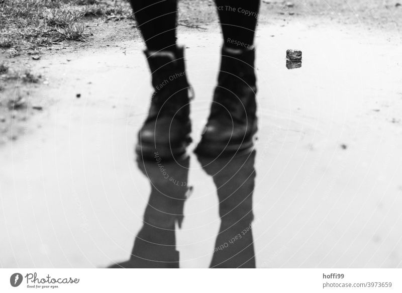 Two legs in boots in the puddle, the stone in the background is in focus Footwear Boots Woman Legs Clothing puddle mirroring Puddle Stand Feminine Fashion