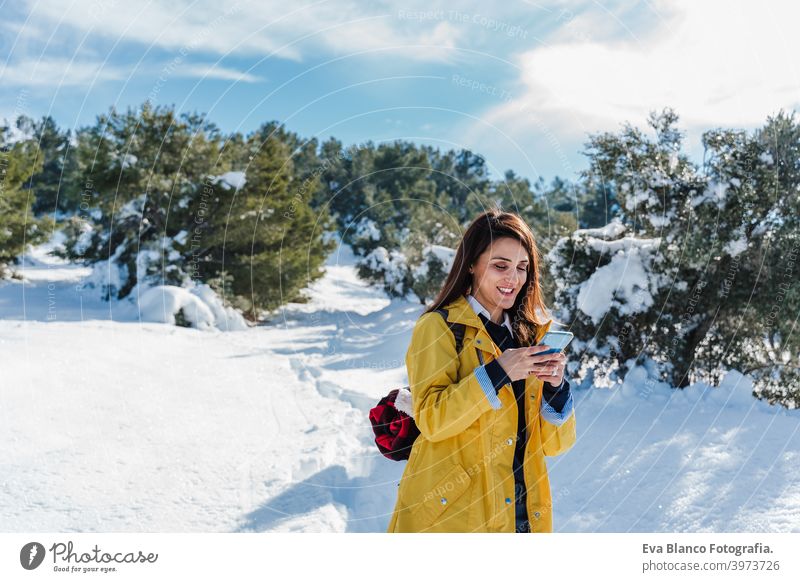 backpacker woman hiking outdoors in snowy mountain. Using mobile phone. Nature, technology and lifestyle internet wireless connection happy yellow coat