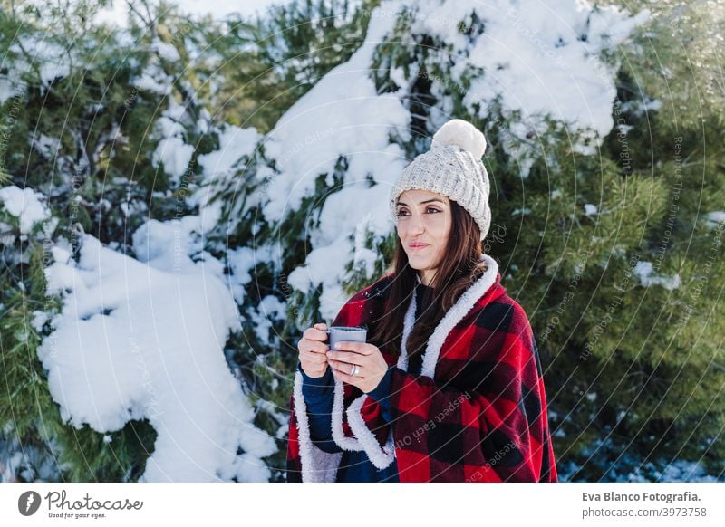 beautiful woman wrapped in plaid blanket holding a cup of hot coffee. nature and lifestyle snow mountain hot tea thermos drink sunny hiking winter cold covered