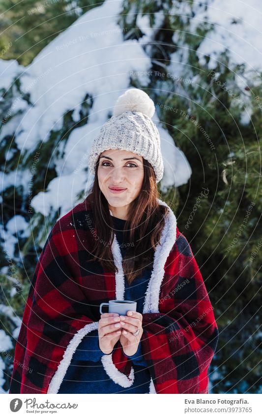 beautiful woman wrapped in plaid blanket holding a cup of hot coffee. nature and lifestyle snow mountain hot tea thermos drink sunny hiking winter cold covered