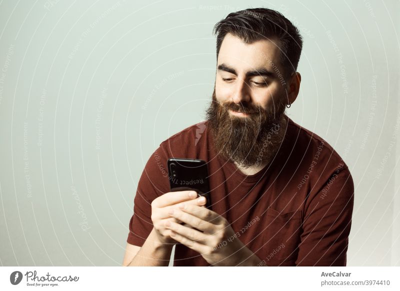 A young hipster style man with a beard and modern haircut smiling while watching his phone screen with copy space laughing colourful living copy-space