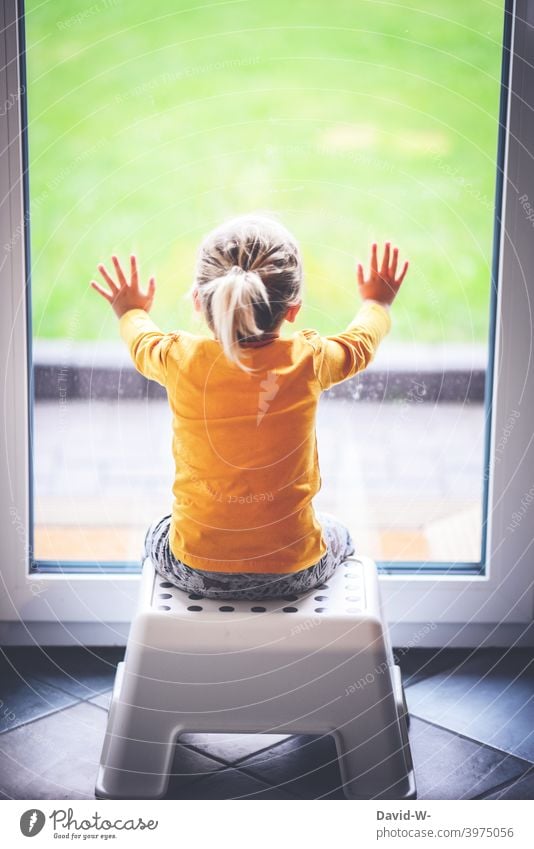 small child sits in front of a closed window and looks longingly outside Child penned Quarantine coronavirus pandemic house arrest Window wistfully stay at home