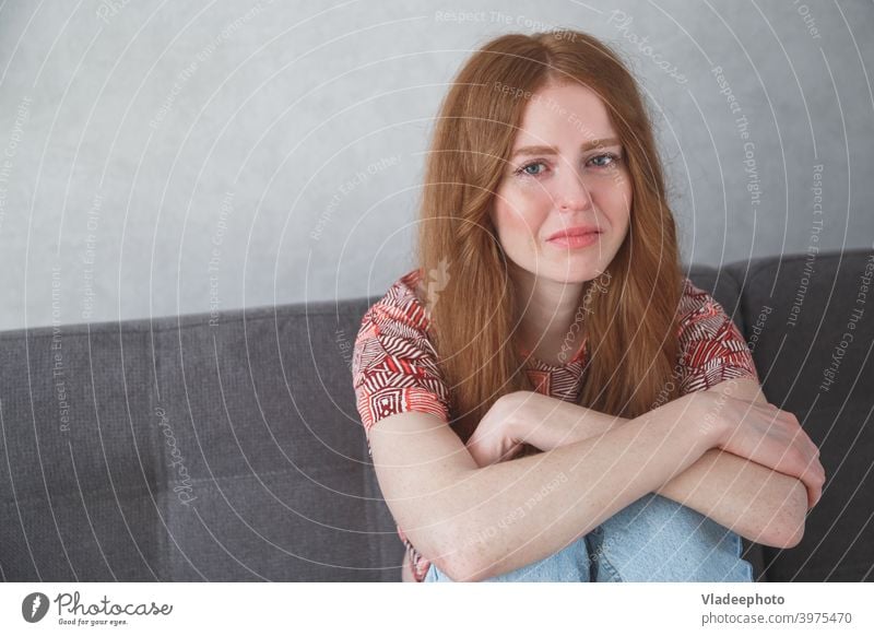 Young sad depressed caucasian woman portrait with tears in her eyes sitting on sofa clasping your knees girl young cry female beautiful sadness face person one