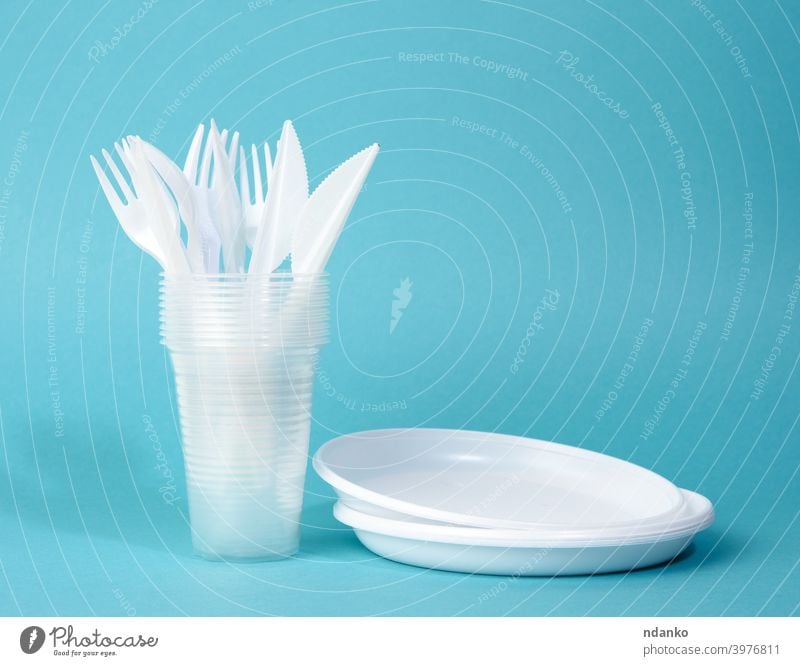 disposable white plastic tableware plates, cups, forks and knives on a blue background service set stack tool utensil circle closeup cutlery dinner dinnerware