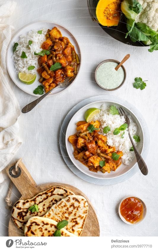 Top down view of a vegetarian, vegan Indian Balti curry with cauliflower and pumpkin served with raita, naan bread and mango chutney and rice on a white background
