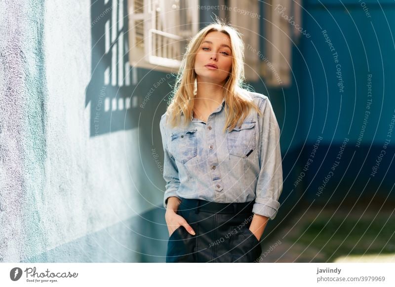 Blonde woman wearing denim shirt and black leather skirt standing in the street. girl female blonde russian blue eyes portrait fashion outdoors lady hairstyle